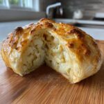 A golden-brown, flaky pastry encases tender cauliflower florets in this Cauliflower Wellington, cut in half on a wooden board.