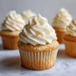 Close-up of a Champagne cupcake topped with swirls of creamy buttercream frosting and edible gold glitter.