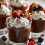 Close-up of a decadent chocolate mousse cup topped with whipped cream, fresh raspberries, strawberries, and blueberries.