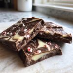 Close-up of three pieces of swirled chocolate and white chocolate peppermint bark with crushed candy cane pieces.