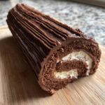 A slice of chocolate Yule Log (Bûche de Noël) with creamy filling, covered in chocolate frosting.