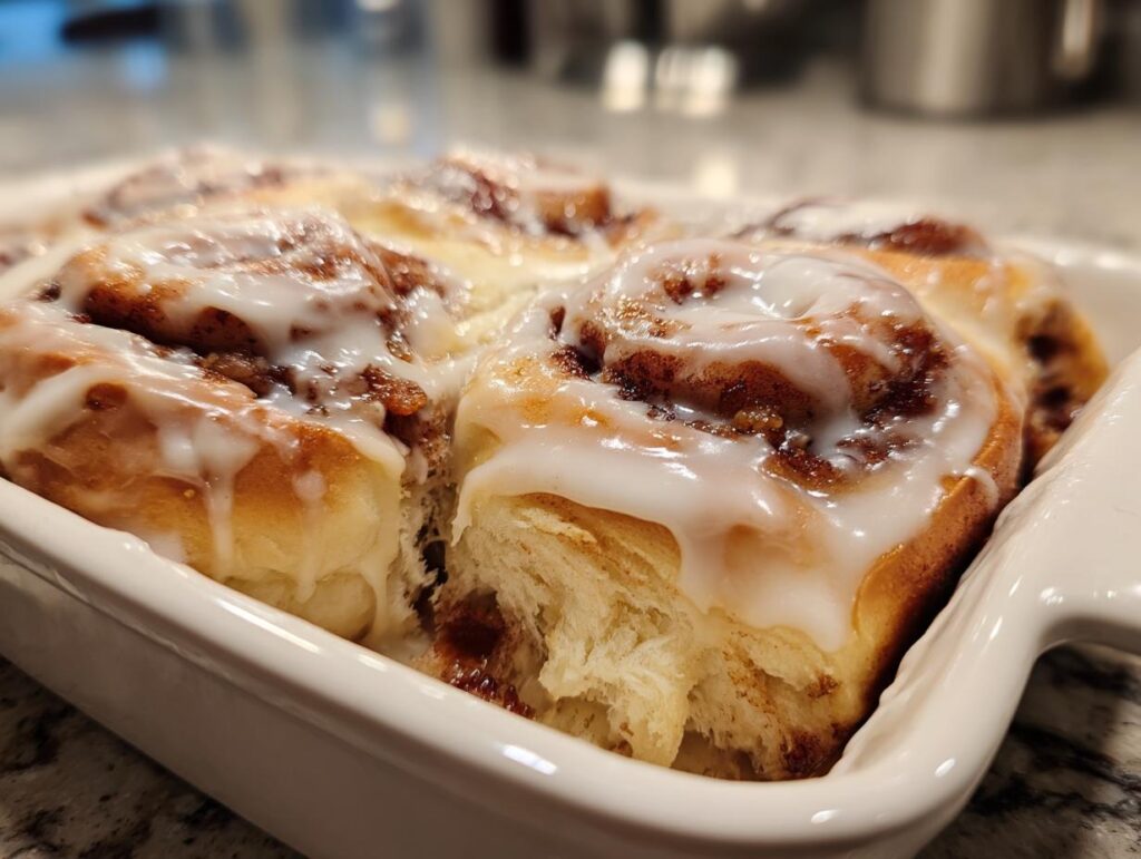Close-up of warm Christmas Morning Cinnamon Rolls with a generous cream cheese glaze in a white baking dish.