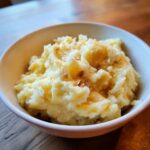 A close-up of a bowl filled with creamy garlic mashed potatoes, topped with melted butter and crispy garlic bits.