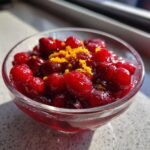 Close-up of fresh cranberry-orange sauce in a glass bowl, topped with orange zest.