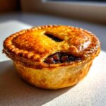 Close-up of a golden-brown mince pie with a flaky crust and visible fruit filling.