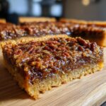 Close-up of a gooey pecan pie bar slice, showcasing the flaky crust and rich, nutty filling.