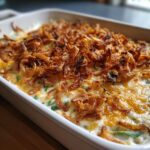 A close-up of a Homestyle Green Bean Casserole topped with golden fried onions and melted cheese.