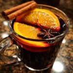 A close-up of a glass mug filled with warm Mulled Wine (Glögg), garnished with orange slices, cinnamon sticks, and star anise.