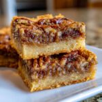 A close-up stack of two Pecan Pie Bars, showcasing a buttery crust and gooey pecan filling.