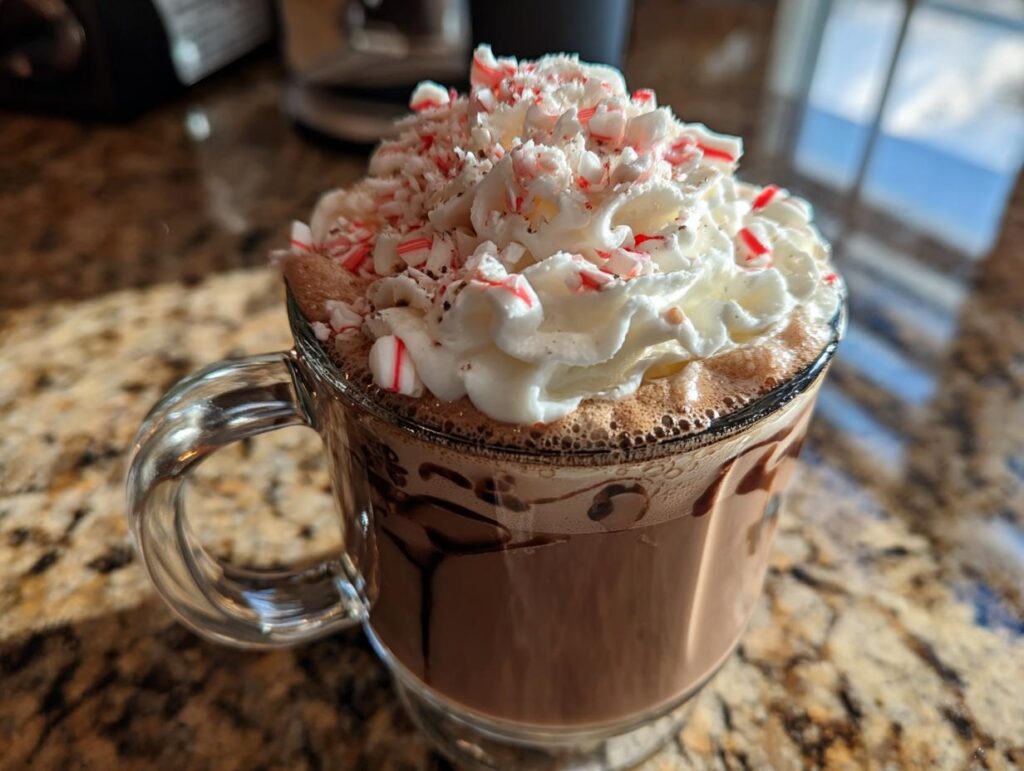 A festive Peppermint Mocha topped with whipped cream and crushed candy canes in a clear mug.