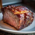 A juicy, perfectly roasted Prime Rib (Standing Rib Roast) resting on a white plate, showcasing its browned crust and pink interior.
