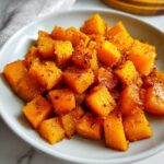 Close-up of roasted butternut squash cubes coated in maple syrup and cinnamon, served in a white bowl.