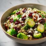 A close-up of a vibrant Winter Salad featuring Brussels sprouts, quinoa, dried cranberries, feta cheese, and pecans.