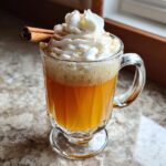 A glass of Apple Cider Chai Fusion topped with whipped cream and a cinnamon stick.