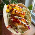 Close-up of a Baked Fish Taco with Mango Salsa, drizzled with sauce and crema.