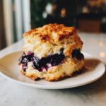 Close-up of a delicious Blueberry Biscuit, filled with blueberry compote, on a white plate.