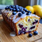 Delicious Blueberry Lemon Pound Cake, topped with blueberries and glaze, on a wooden board.