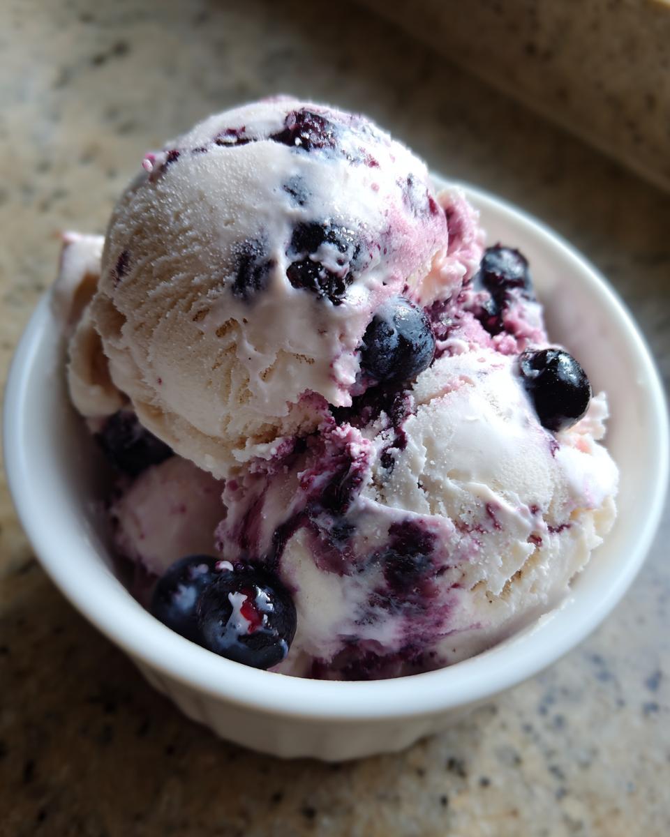 Close-up of a bowl with scoops of blueberry yogurt ice cream, showing the creamy texture and fresh blueberries.