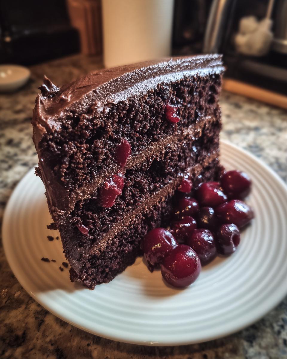 A slice of Chocolate Cherry Torte on a white plate, topped with fresh cherries.