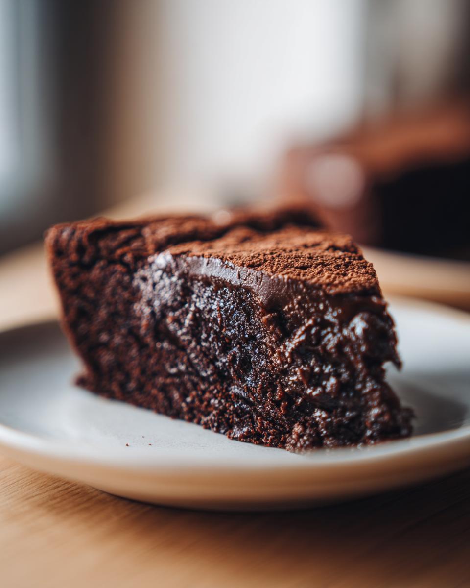 A slice of decadent Chocolate Fudge Cake on a white plate, ready to be enjoyed.