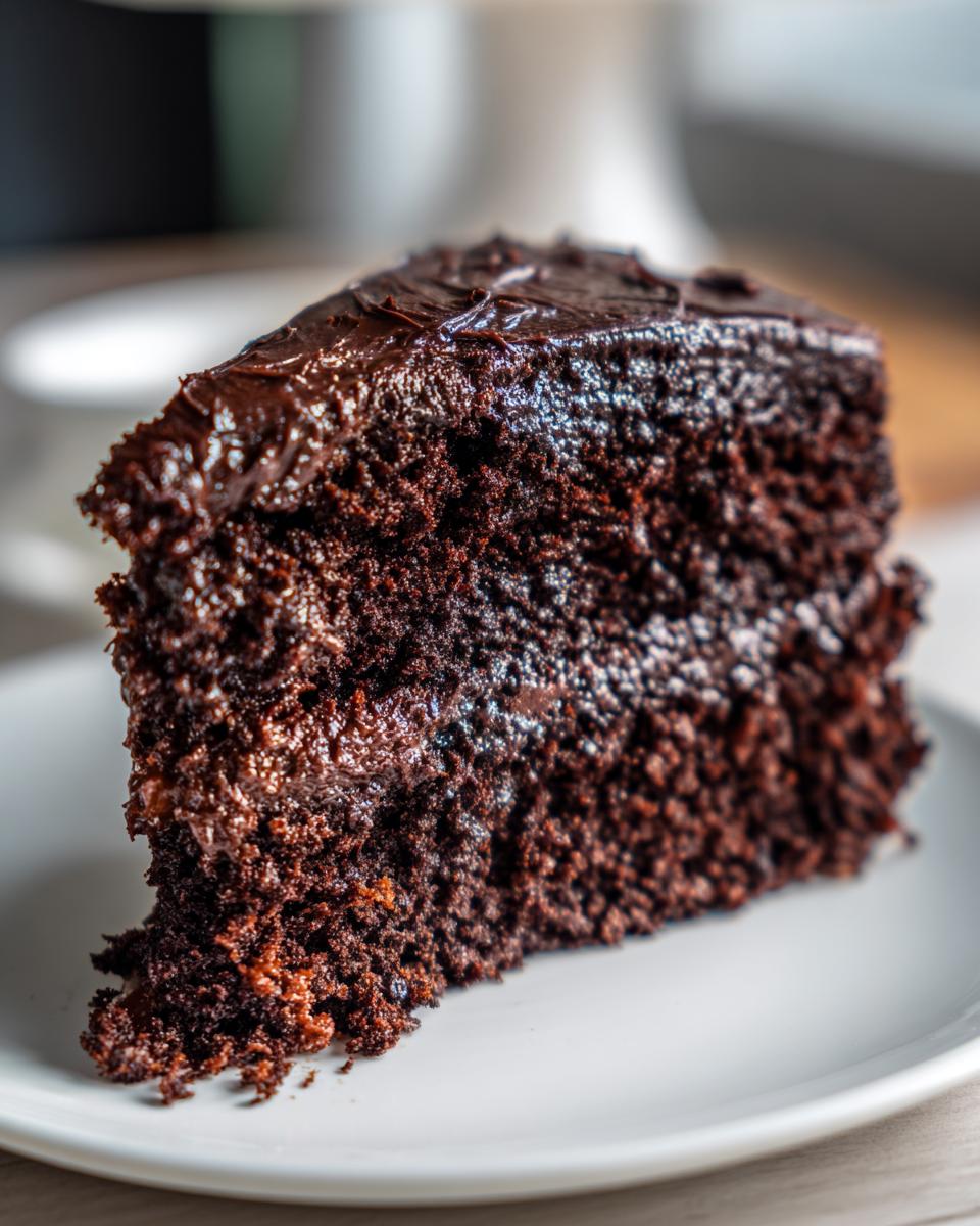 Close-up of a slice of rich Chocolate Mayonnaise Cake on a white plate, showing moist texture.