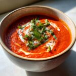 A bowl of creamy roasted tomato soup, garnished with fresh basil and cream.