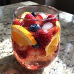Close-up of a glass filled with Cupid's Pink Rosé Sangria, featuring fresh fruit and ice.