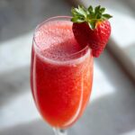 Close-up of a frosty Easy Frosty Strawberry Mimosa in a champagne flute, garnished with a fresh strawberry.