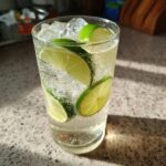 A tall glass of Elderflower Spritzer with ice and lime slices.