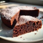 A slice of delicious flourless chocolate cake dusted with powdered sugar, next to the whole cake.