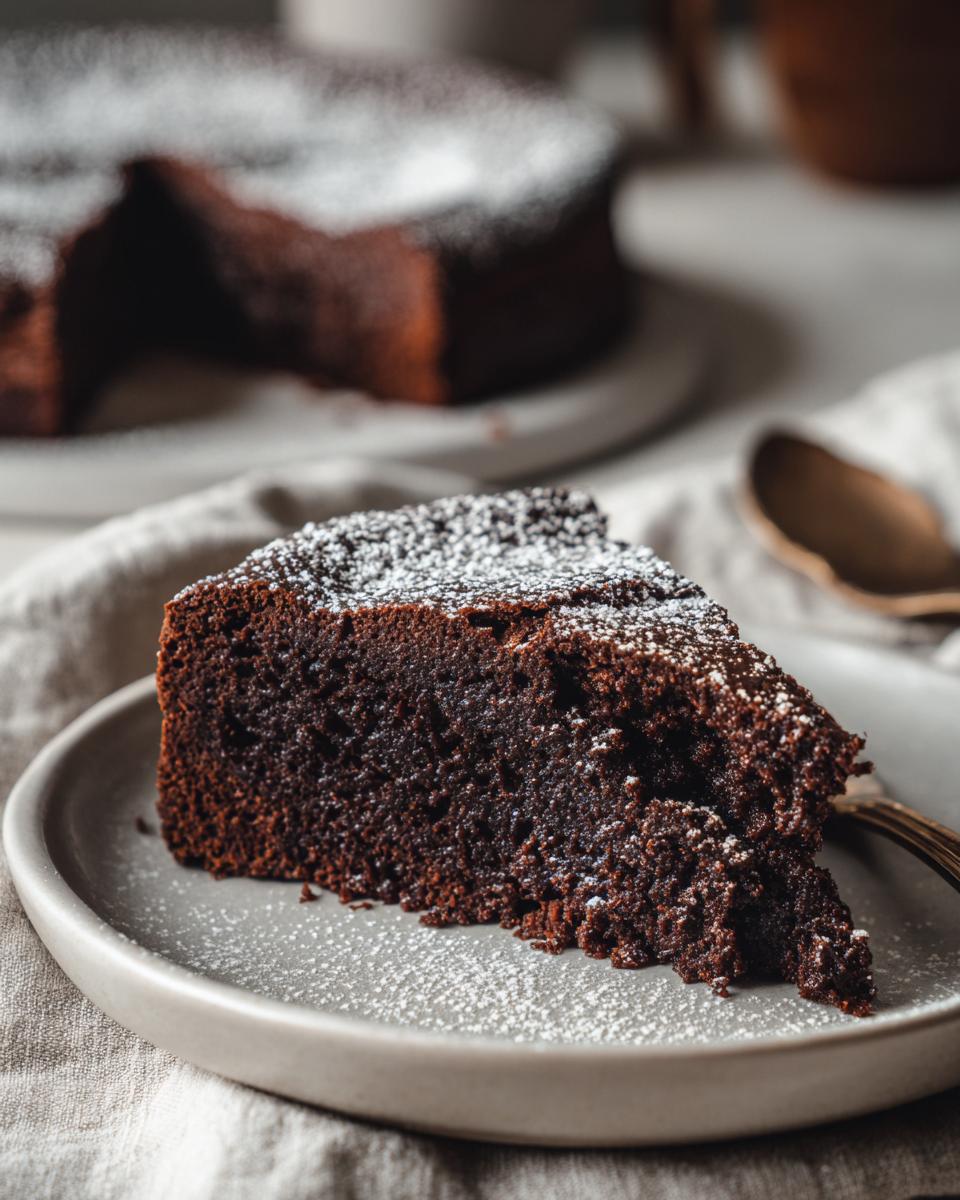 A slice of delicious flourless chocolate cake on a plate, dusted with powdered sugar.