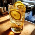 A tall glass of Ginger Lemon Sparkle cocktail with ice and lemon slices, bubbly and refreshing.