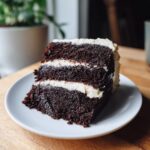 A slice of delicious Guinness Chocolate Cake on a white plate, showing layers of cake and frosting.