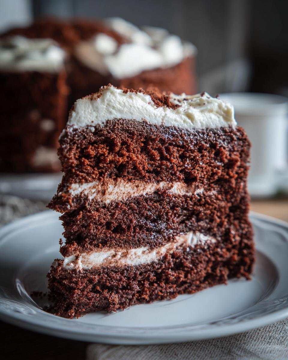 A delicious slice of Guinness Chocolate Cake on a white plate, showing layers and frosting.