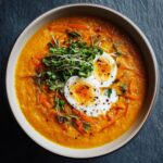 Overhead shot of a bowl of Immune-Boosting Carrot Ginger Soup, garnished with microgreens and egg.