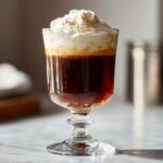 A tall glass of Irish Coffee with whipped cream, showcasing the layers of coffee and whiskey.