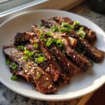 Slices of Korean Beef Bulgogi on a white plate, garnished with sesame seeds and green onions.