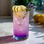A tall glass of Lavender Lemonade garnished with lemon slices and lavender sprigs.