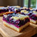 Close-up of a slice of Lemon Blueberry Bars on a wooden board, dusted with powdered sugar.