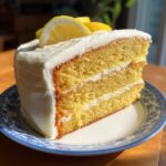 A slice of Lemon Lavender Layer Cake on a plate, topped with lemon slices and frosting.