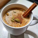 Close-up of a steaming cup of The Perfect Stovetop Chai Latte with cinnamon and cardamom.