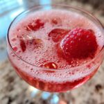 Close-up of a Prosecco Pink Velvet Fizz cocktail, garnished with a fresh raspberry.