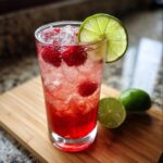 A vibrant Raspberry Lime Rickey cocktail with fresh raspberries, lime, and ice in a tall glass.