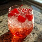 Close-up of a Shirley Temple Punch in a glass with ice and cherries.