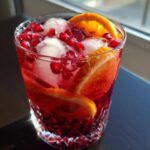 Close-up of a glass of Sparkling Pomegranate Sangria with pomegranate seeds and orange slices.