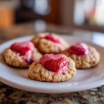 Close-up of a plate of Strawberry Kiss Cookies, with fresh strawberries on top.