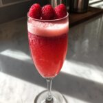 A refreshing Valentine's Day Raspberry Bellini garnished with fresh raspberries.