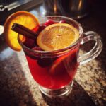 A glass of warm spiced cranberry-apple punch with orange slices and cinnamon stick.
