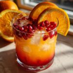 Close-up of a Winter Sunrise Mocktail with orange slices and pomegranate seeds.