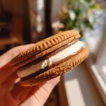 Close-up of a delicious Baileys Irish Cream Sandwich Cookie held in a hand, showing the layers of cream.